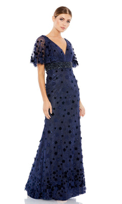A woman wears the Mac Duggal 67712 short-sleeve long formal dress, a floor-length navy gown with a deep V-neckline, flutter sleeves, and elegant floral embellishments.