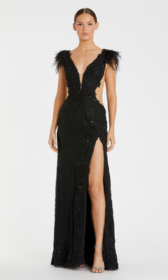 A woman models the Mac Duggal 67782 Black Embroidered Formal Gown, featuring a deep V-neckline, feathered shoulders, side cutouts, floral embroidery, and a high slit, standing against a plain white background.