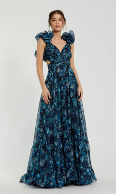 A woman stands against a plain light background wearing the Mac Duggal 67803 Ruffled Long Print Formal Dress, a floor-length, dark blue floral gown with ruffled shoulder details.