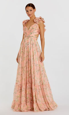 A woman models the Mac Duggal 67803 Ruffled Long Print Formal Dress, featuring a floor-length peach floral print, ruffled shoulders, and a deep V-neckline against a plain white background.