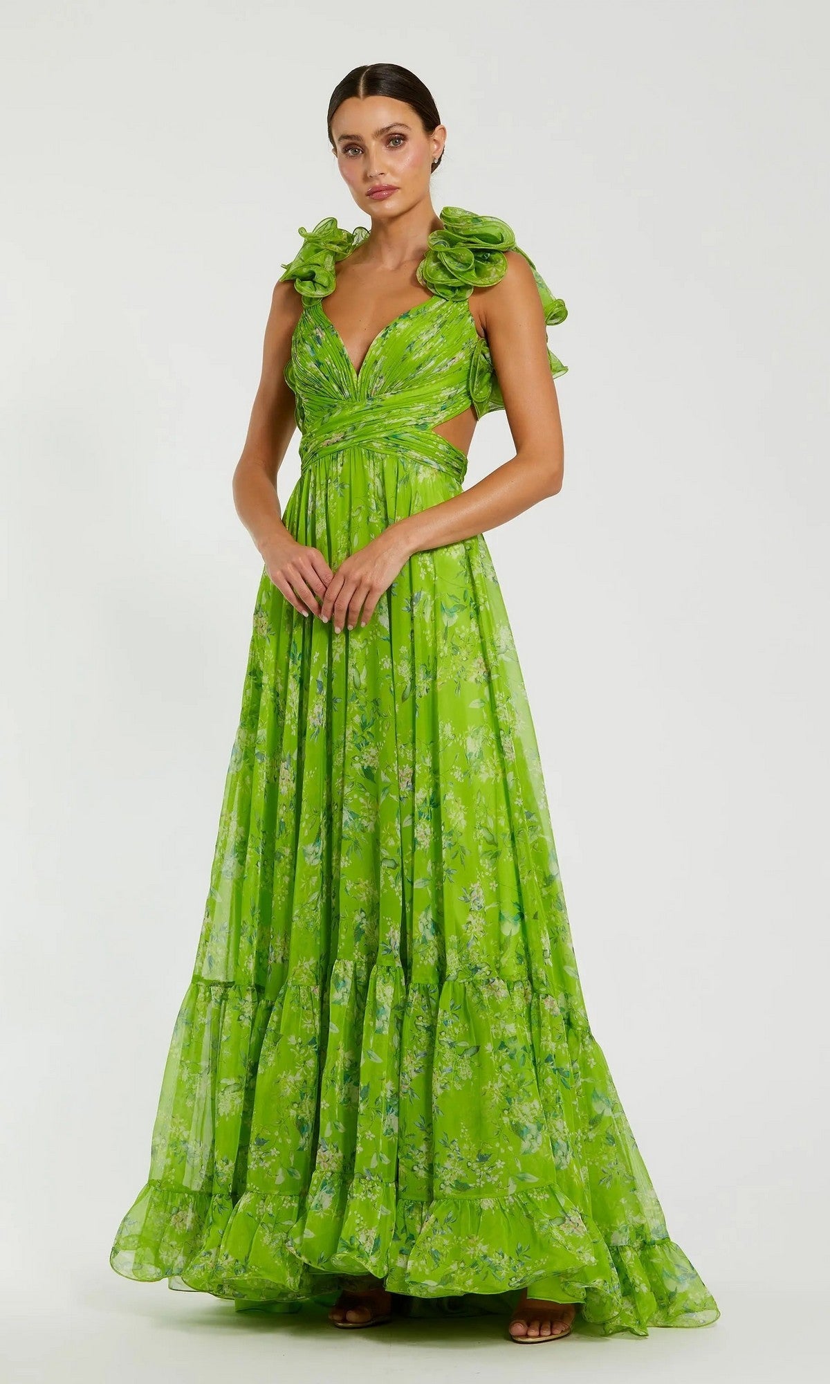 A woman in the Mac Duggal 67803 Ruffled Long Print Formal Dress, featuring florals, ruffled shoulders, and waist cutouts, stands against a plain light background.