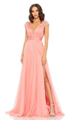A woman wears the Coral Pink Cap Sleeve Long Prom Gown 67811, featuring beaded cap sleeves, a deep V-neckline, and a thigh-high slit, paired with nude high-heeled sandals.