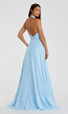 A woman wearing the Mac Duggal 67816 open-back halter formal dress in light blue stands facing away, looking over her shoulder.