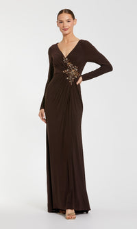 A woman poses against a plain background in the Mac Duggal 67848 Long Sleeve Long Formal Dress, a floor-length dark brown evening gown featuring a V-neck and beaded waist embellishment, with one hand on her hip.