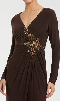 A woman stands against a plain background in the Mac Duggal 67848, a long sleeve formal dress featuring a V-neck and gold and brown beaded waist embellishments.