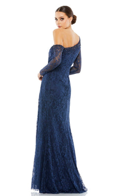 A woman wears the Long Formal Dress 67852 by Mac Duggal, a floor-length, off-the-shoulder navy lace gown with an embellished neckline and long sleeves, posing as she looks over her shoulder.