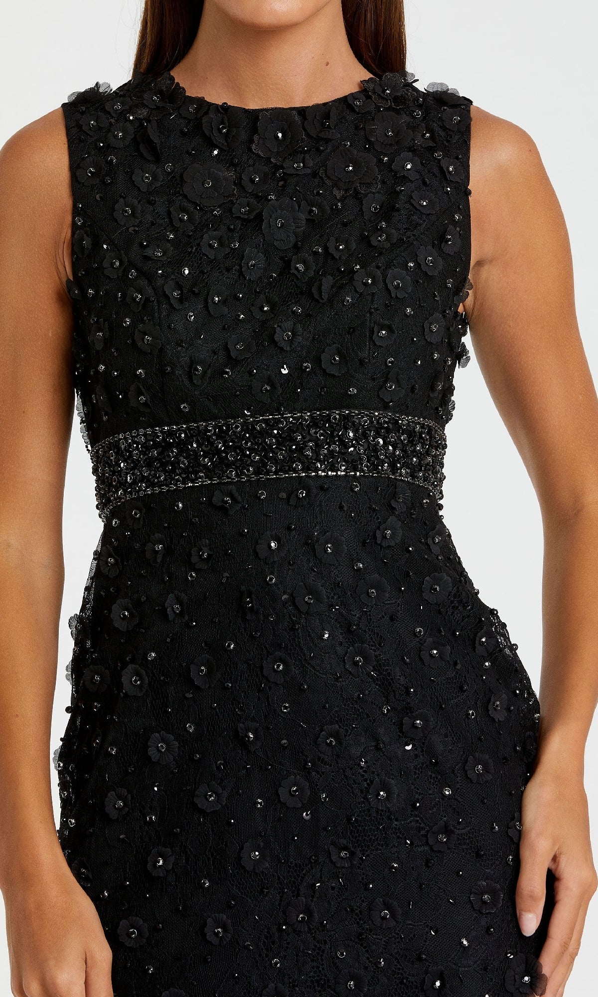 A woman wears the Mac Duggal 67853 knee-length party dress, a sleeveless black design with textured floral patterns and beaded embellishments on the waist and bodice.