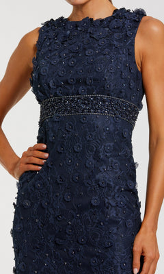 A person poses with one hand on their hip, wearing the Mac Duggal 67853 knee-length party dress—a sleeveless navy blue midi featuring beaded embellishments and floral lace details at the waist.
