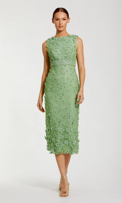 A woman wears the Mac Duggal 67853 knee-length party dress in light green lace with floral detailing and open-toe heels, standing against a plain background.