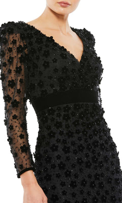 A woman models the Short Wedding Guest Dress 67856 by Mac Duggal—black, semi-formal with sheer sleeves, floral appliqué, and a V-neckline. Shown from mid-face to mid-thigh; ideal for weddings or special occasions.