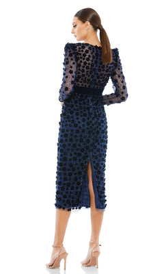 Wearing the Short Wedding Guest Dress 67856 by Mac Duggal—a navy blue, long-sleeved, knee-length floral embellished dress with a back slit—a woman in nude heels poses with her back to the camera, ideal for semi-formal events.