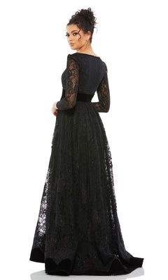 A woman stands looking over her shoulder, wearing the Mac Duggal 67861 long black lace formal dress with long sleeves and a black belt.