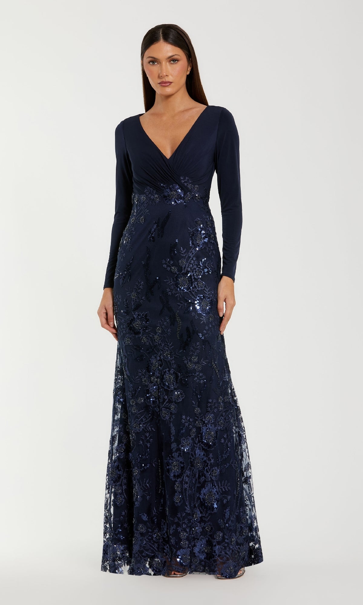 A woman wears the Mac Duggal 67871 Long Sleeve Dark Blue Formal Gown, featuring a V-neckline and sparkling floral sequins.