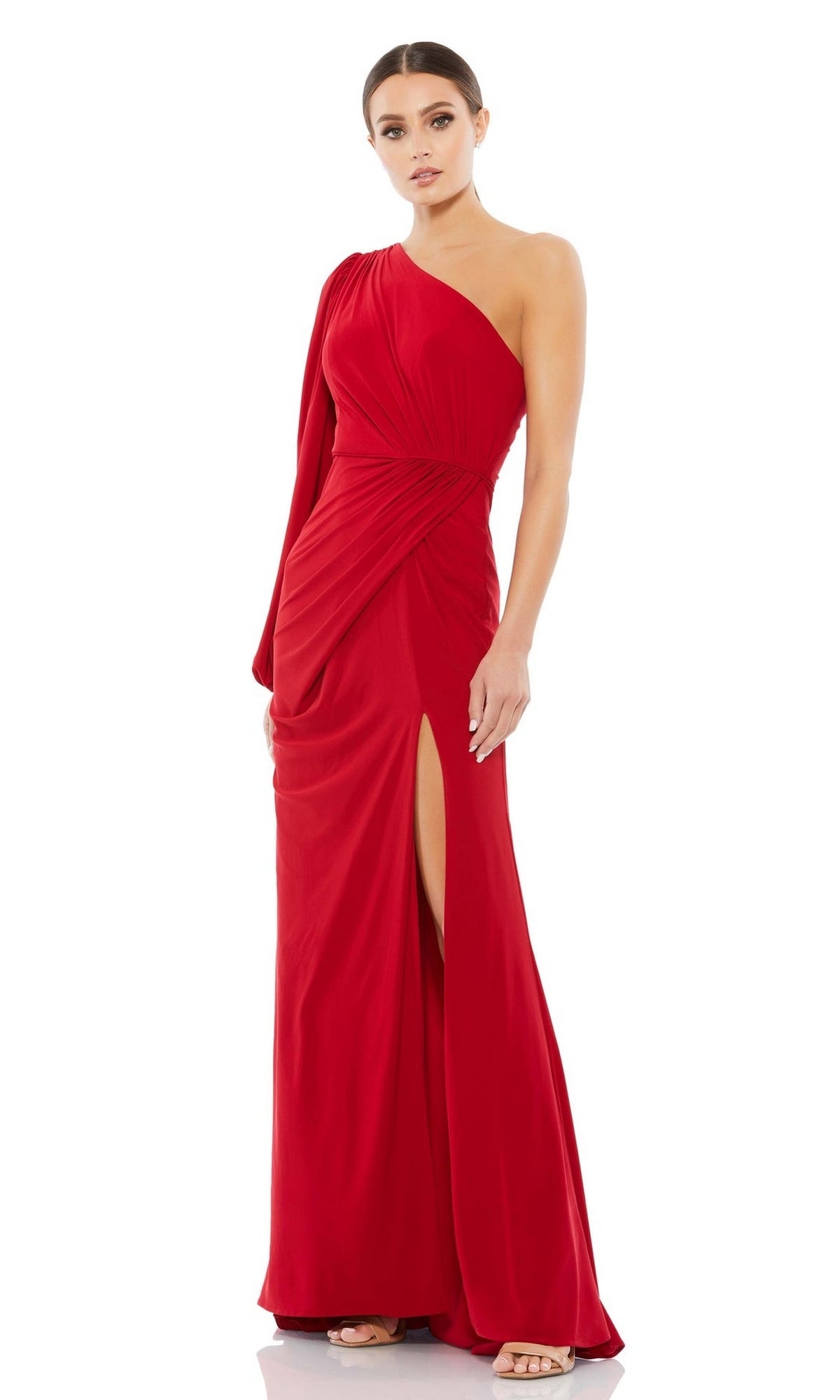 A woman wears the Mac Duggal 67879, a floor-length asymmetrical formal dress in vibrant red with a side slit. Her hair is pulled back, and she pairs the look with open-toed shoes.
