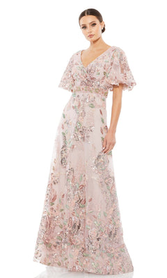 A woman wears the Mac Duggal 67880 Short Sleeve Pink Formal Dress, featuring flutter sleeves and floral sequin embellishments. This elegant gown drapes to the floor, perfect for special occasions.