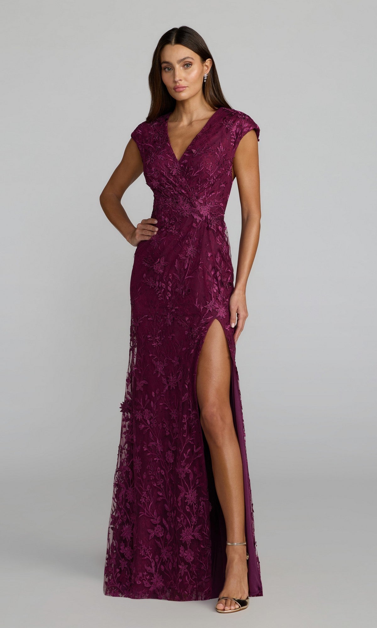 A woman wearing a cap sleeve, floor-length blue Mac Duggal 67882 formal gown, standing against a plain background.