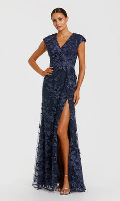 A woman models the Mac Duggal 67882 long formal dress in midnight, showcasing floral lace, cap sleeves, a V-neckline, embroidered mesh overlay, and a high front slit, paired with silver strappy heels.