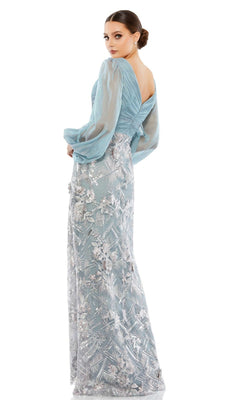 A woman stands against a white background wearing the Mac Duggal Long Formal Dress 67886 in slate blue, featuring sheer puff sleeves and a floral lace overlay on the floor-length skirt.