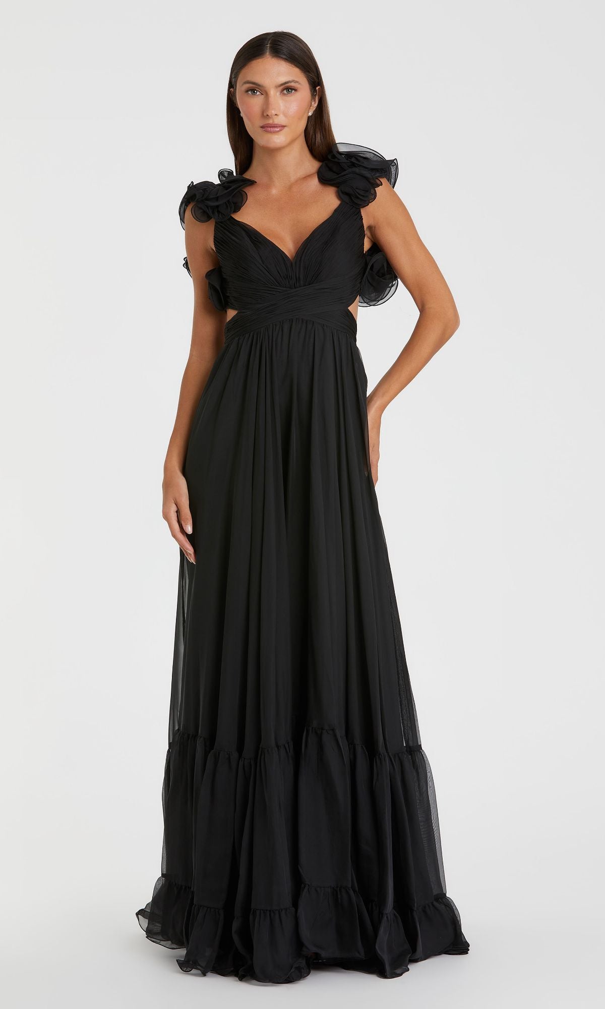 A woman poses against a plain white background wearing the Mac Duggal Empire-Waist Cut-Out Formal Dress 67911, a long black sleeveless gown with ruffled shoulders and a gathered skirt.
