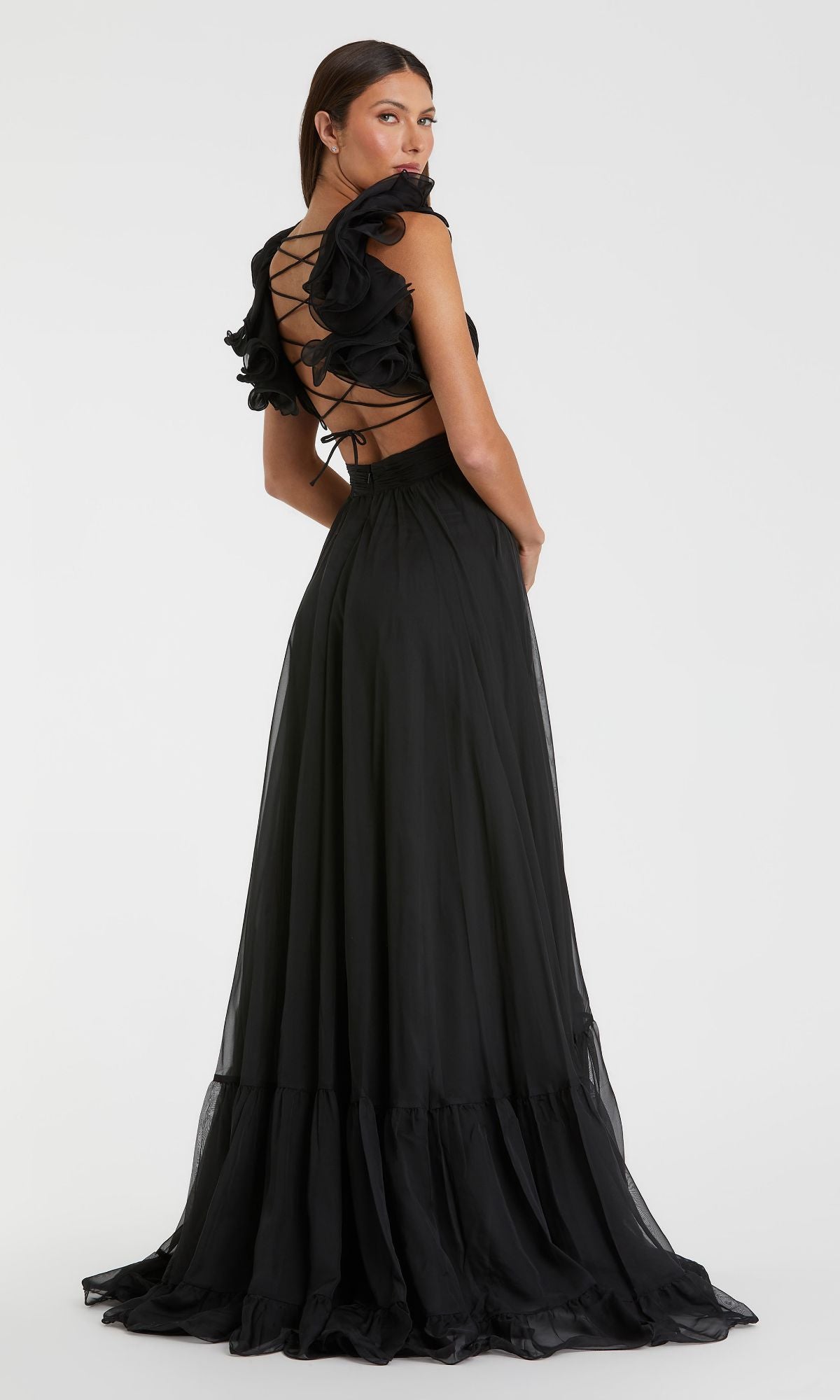 A woman faces away, wearing the Mac Duggal Empire-Waist Cut-Out Formal Dress 67911—a long black gown featuring ruffled sleeves, an elegant open back, and striking lace-up details.