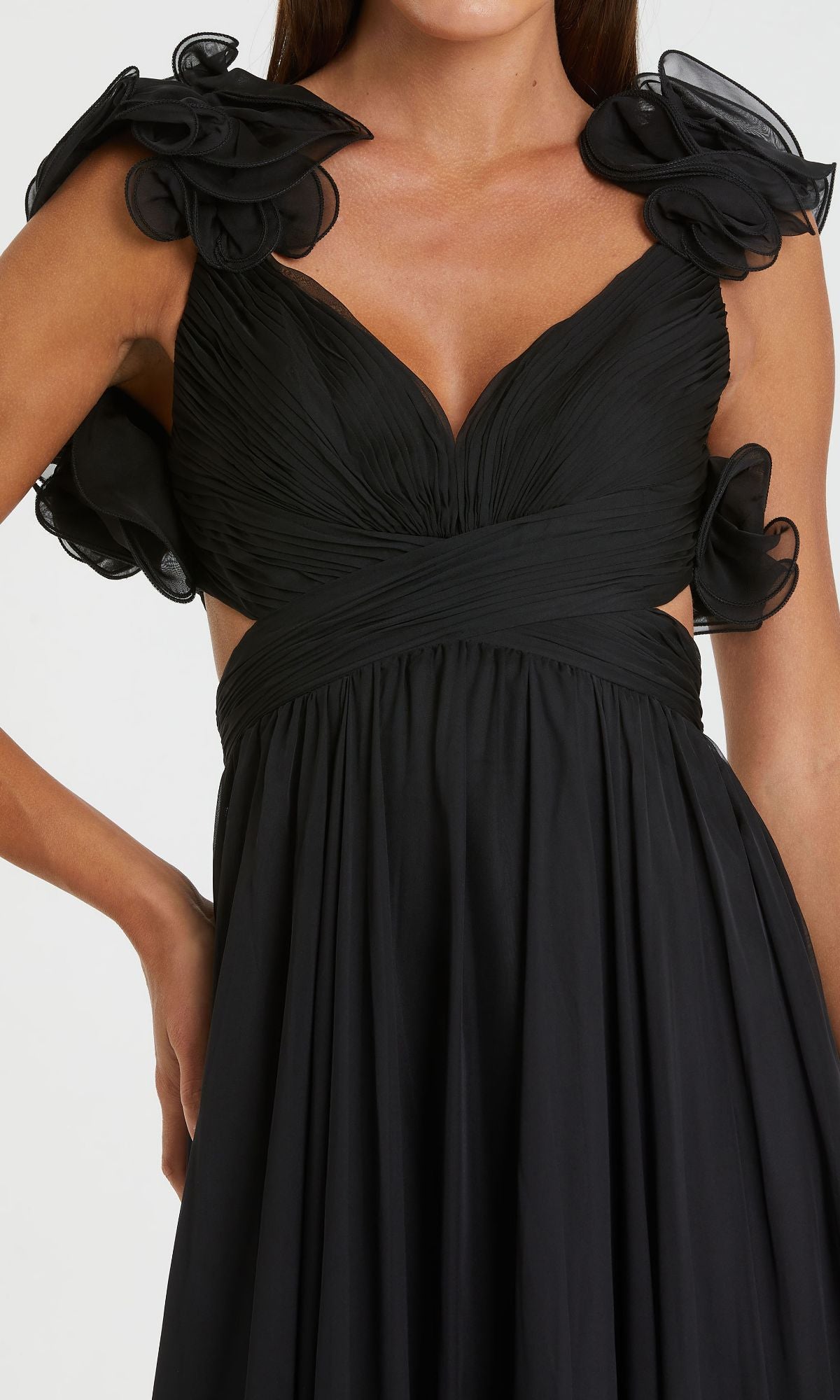 Woman wearing the Mac Duggal Empire-Waist Cut-Out Formal Dress 67911, a sleeveless black v-neck gown featuring a pleated bodice, floral ruffle shoulders, cutout sides, and a deep neckline.