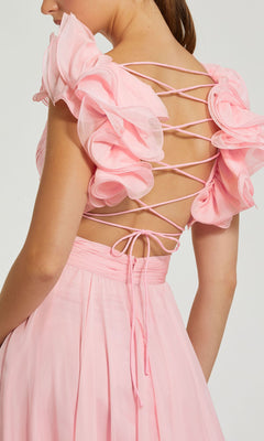 A person wearing the Mac Duggal Empire-Waist Cut-Out Formal Dress 67911, featuring a light pink hue, v-neckline, ruffled sleeves, and a crisscross lace-up back detail.