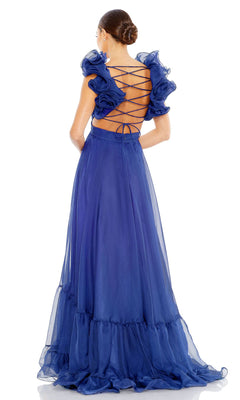 A woman stands with her back to the camera, wearing the Mac Duggal Empire-Waist Cut-Out Formal Dress 67911—a floor-length royal blue gown featuring a lace-up open back and ruffled sleeves.