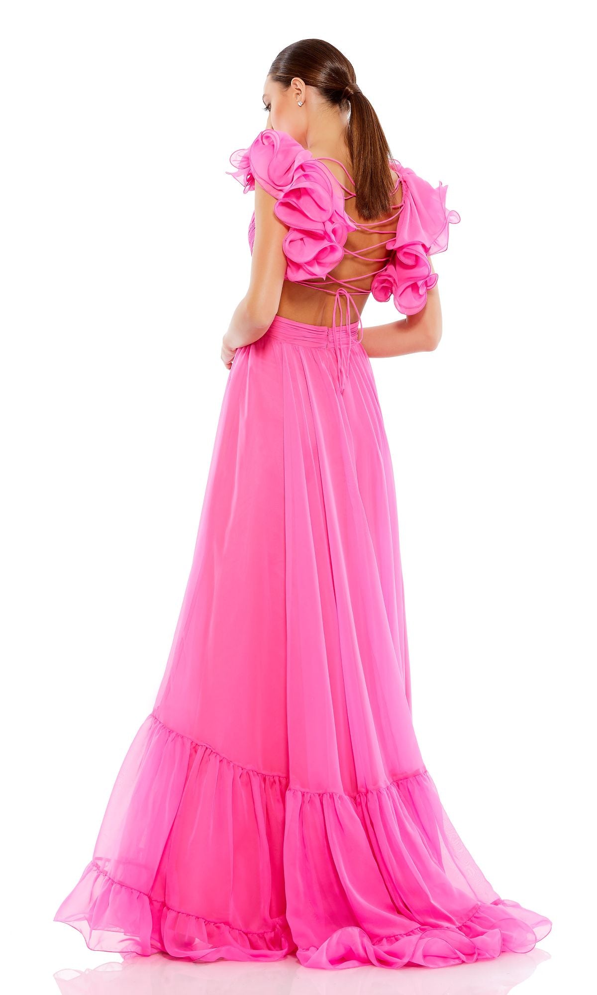 A woman poses against a white background in the Mac Duggal Empire-Waist Cut-Out Formal Dress 67911—a long, bright pink gown featuring lace-up open back and ruffled sleeves.