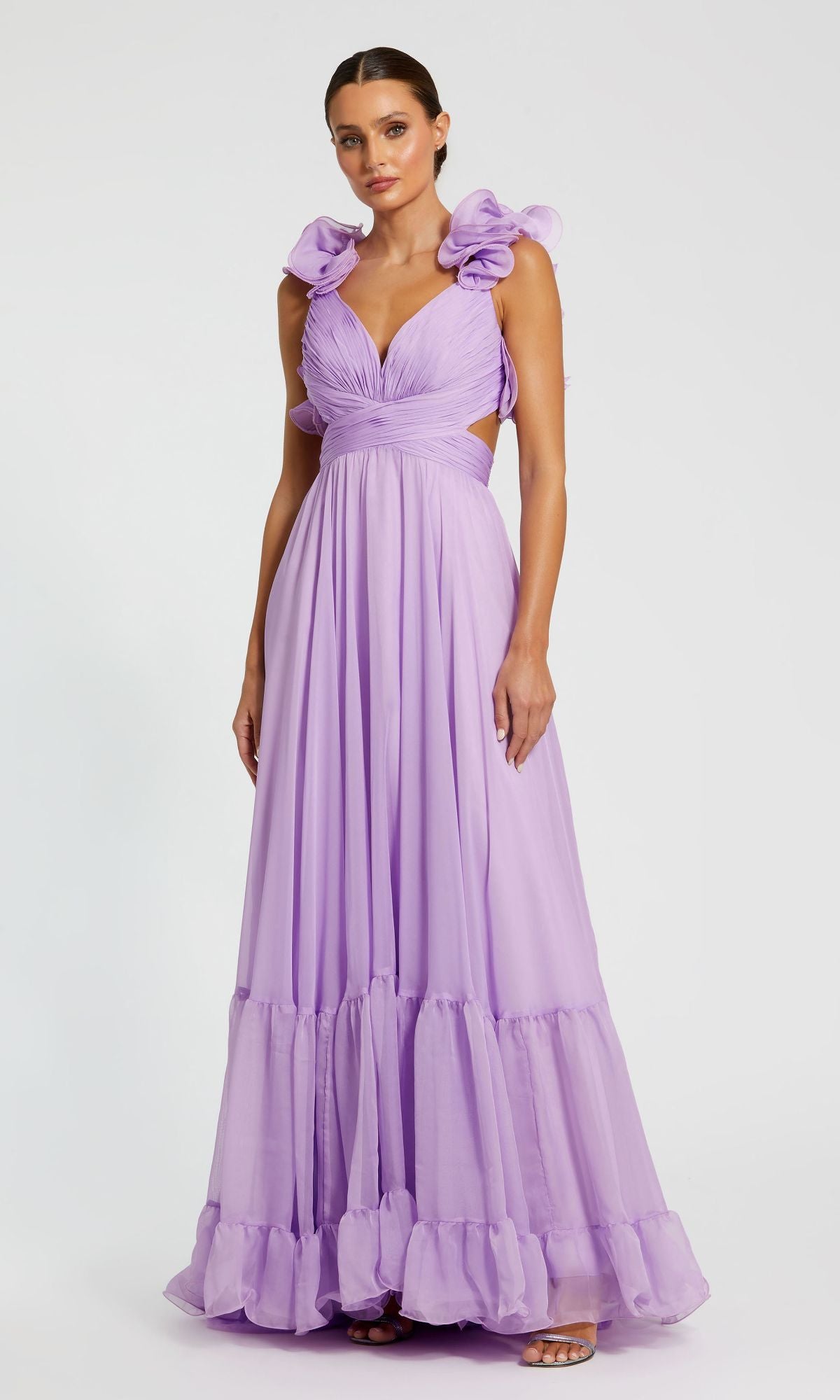 A woman wears the Mac Duggal Empire-Waist Cut-Out Formal Dress 67911, a long lavender gown with ruffled shoulders and a deep V-neck, standing against a plain white background.