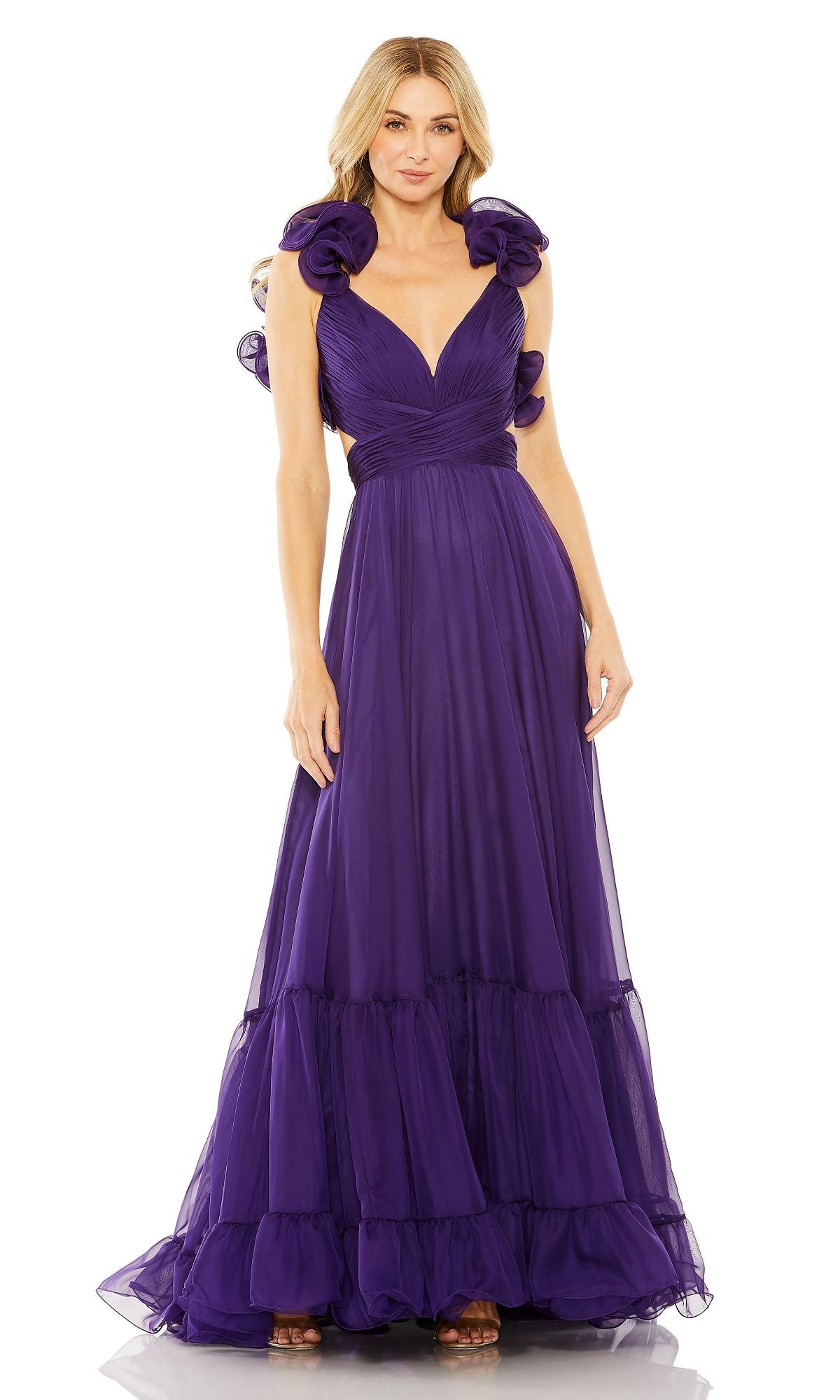 A woman stands against a white background wearing the Mac Duggal Empire-Waist Cut-Out Formal Dress 67911, a floor-length deep purple gown featuring a v-neckline, ruffled shoulder details, and a fitted bodice.
