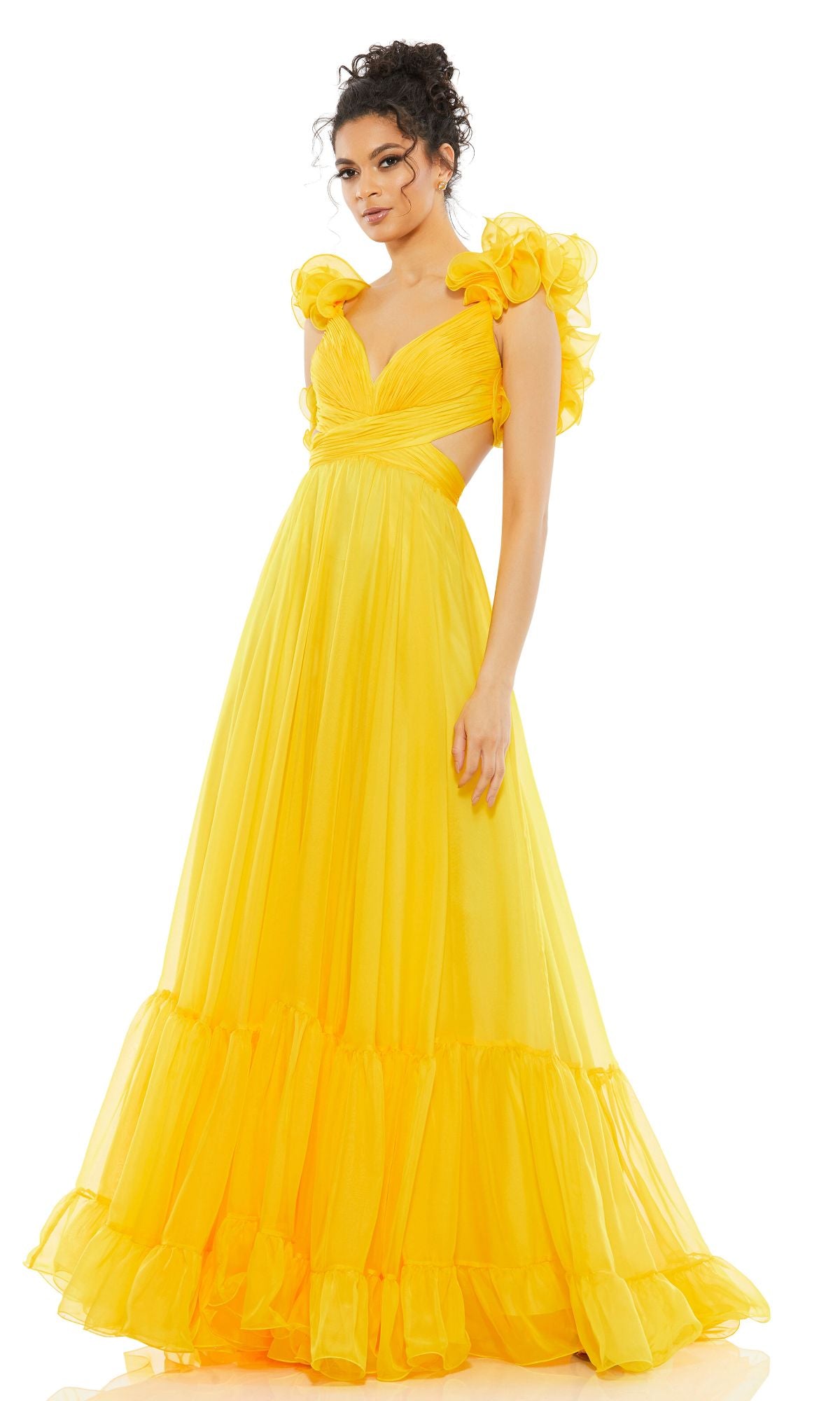 A woman models the Mac Duggal Empire-Waist Cut-Out Formal Dress 67911, a bright yellow, floor-length gown with v-neckline, ruffled shoulders, and a voluminous skirt, standing against a plain white background.