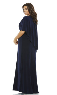 A woman with long brown hair models the Long Plus-Size Prom Dress 67929 by Mac Duggal, featuring cape sleeves and a floor-length design, as she stands looking over her shoulder.