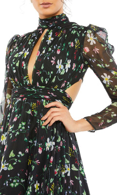 A woman poses with one hand on her hip, wearing the Mac Duggal 67942 Long Black Print Formal Dress featuring sheer long sleeves, a high neck, cut-out sides, and a black floral print.
