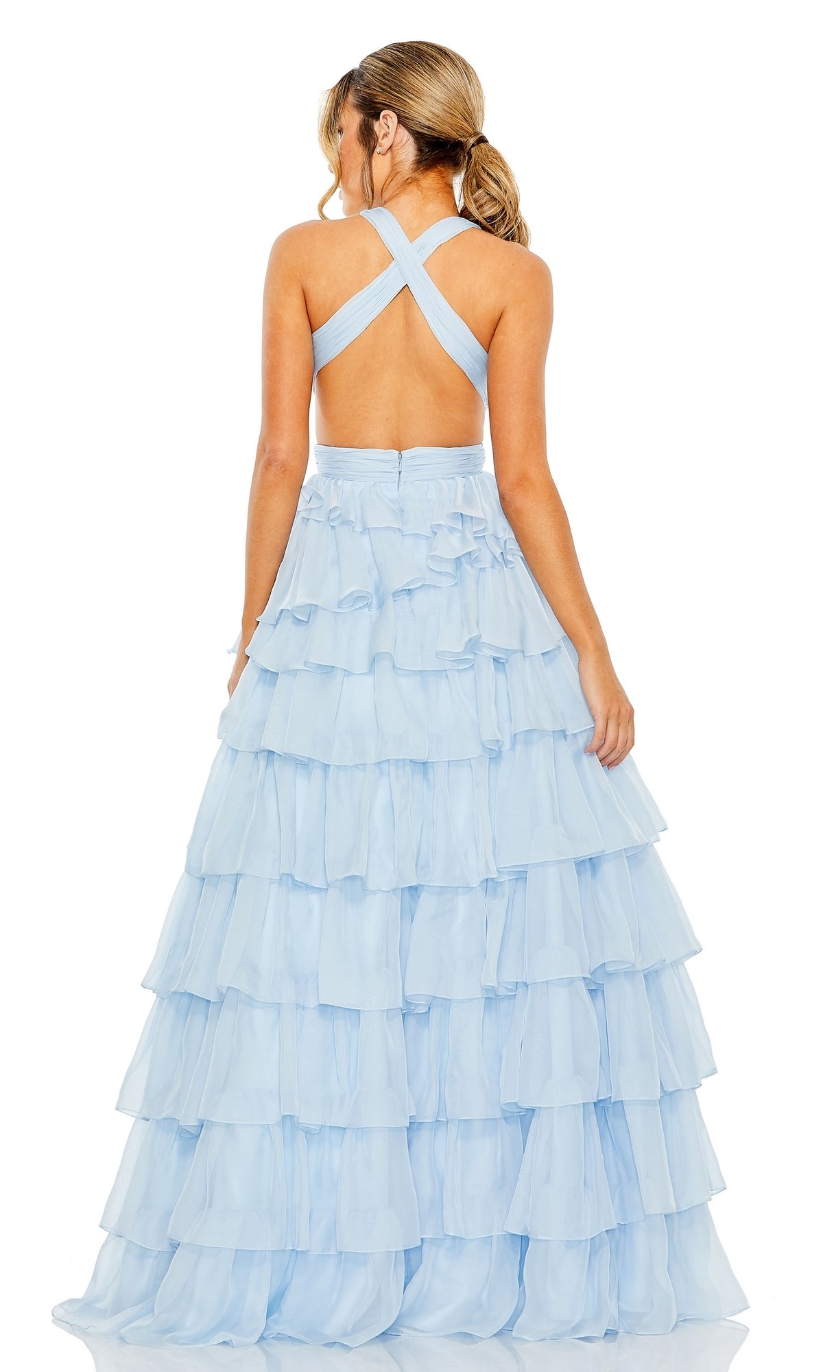 A woman stands with her back to the camera in the Long Formal Dress 67988 by Mac Duggal, featuring a light blue tiered ruffle A-line ball gown, v-neckline, and crisscross open back.