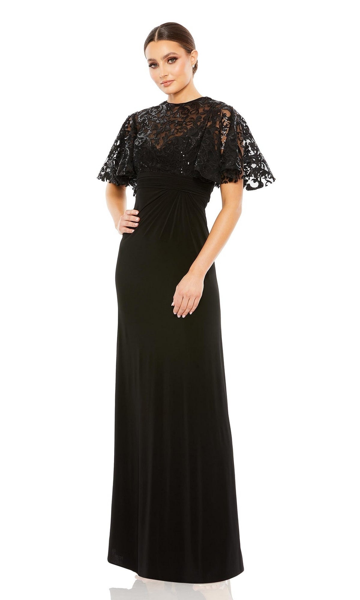A woman wears the Mac Duggal 68002 Short Sleeve Black Formal Dress, featuring a fitted waist and sequin-lace sleeves, standing against a white background.