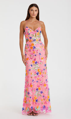 A woman stands against a white background wearing the Mac Duggal 68067 Sequin-Print Pink Formal Dress, a long pink gown with spaghetti straps and colorful floral patterns and sequins.