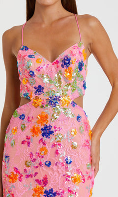 A woman in the Mac Duggal 68067 sequin-print pink formal dress, featuring colorful floral details, stands with one hand on her hip.