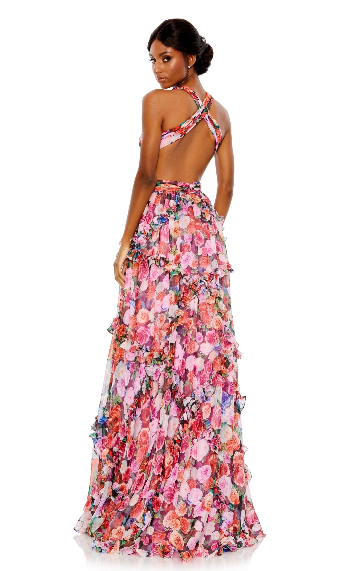 A woman poses against a white background, looking over her shoulder in the Long Formal Dress 68076 by Mac Duggal, featuring a floral print, floor-length design, sleeveless cut, open back, and crisscross straps.