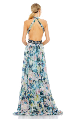 A woman stands facing away, wearing the Mac Duggal Long Formal Dress 68089—a sleeveless, floor-length pastel floral gown with an open back and black waistband.