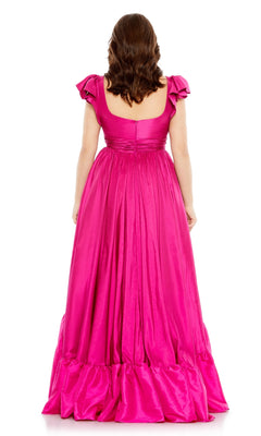 A woman with wavy brown hair models the Long Plus-Size Formal Dress 68150 by Mac Duggal in magenta pink, standing with her back to the camera against a white background.
