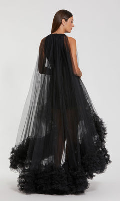 A woman faces away, wearing the Mac Duggal 68252 High-Low Trapeze Formal Dress—sheer black with tulle layers and a ruffled hem—set against a plain white background.
