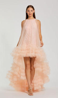 A woman wears the Mac Duggal 68252 High-Low Trapeze Formal Dress in peach tulle with ruffled layers and strappy heeled sandals, standing against a plain background.