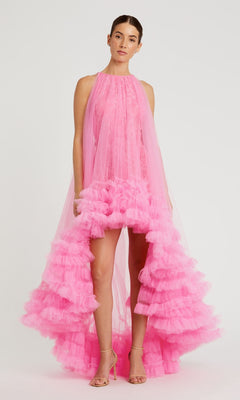 A person stands against a plain background wearing the Mac Duggal 68252 High-Low Trapeze Formal Dress in bright pink with ruffles and lace details, paired with nude heeled sandals.