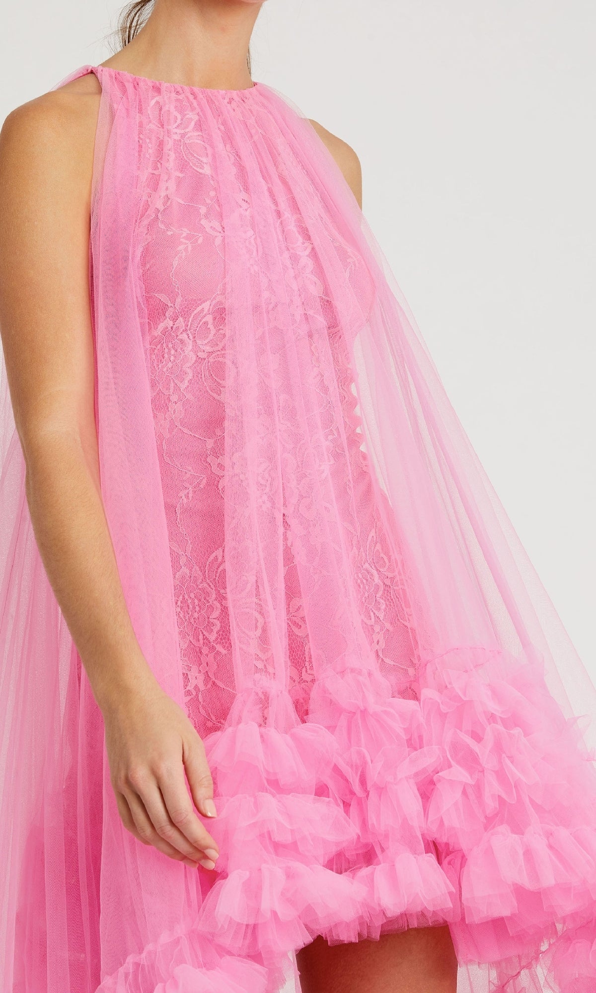 A person wearing the Mac Duggal 68252 High-Low Trapeze Formal Dress, featuring sleeveless pink lace, sheer tulle layers, and a ruffled hem.