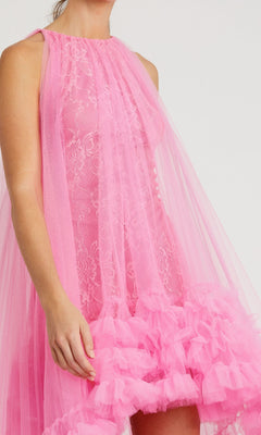 A person wearing the Mac Duggal 68252 High-Low Trapeze Formal Dress, featuring sleeveless pink lace, sheer tulle layers, and a ruffled hem.