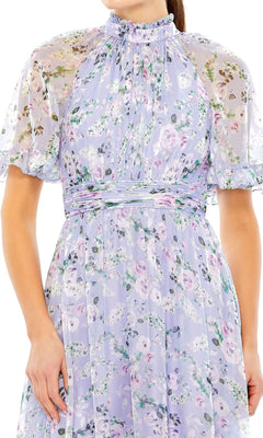 A person wearing the Mac Duggal 68259 Lilac Floral Print Formal Dress featuring sheer flutter sleeves, a high ruffled neckline, and an elegant A-line midi silhouette.