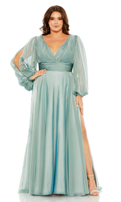 A woman stands confidently with one hand on her hip, wearing the Long Plus-Size Formal Dress 68431 by Mac Duggal: a floor-length, light teal gown with sheer long sleeves, V-neckline, gathered waist, and high leg slit.