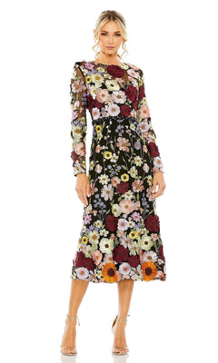 A woman models the Mac Duggal 68462 tea-length wedding-guest dress, featuring black floral print, long sheer sleeves, and colorful embroidery, styled with nude high-heeled sandals against a plain white background.