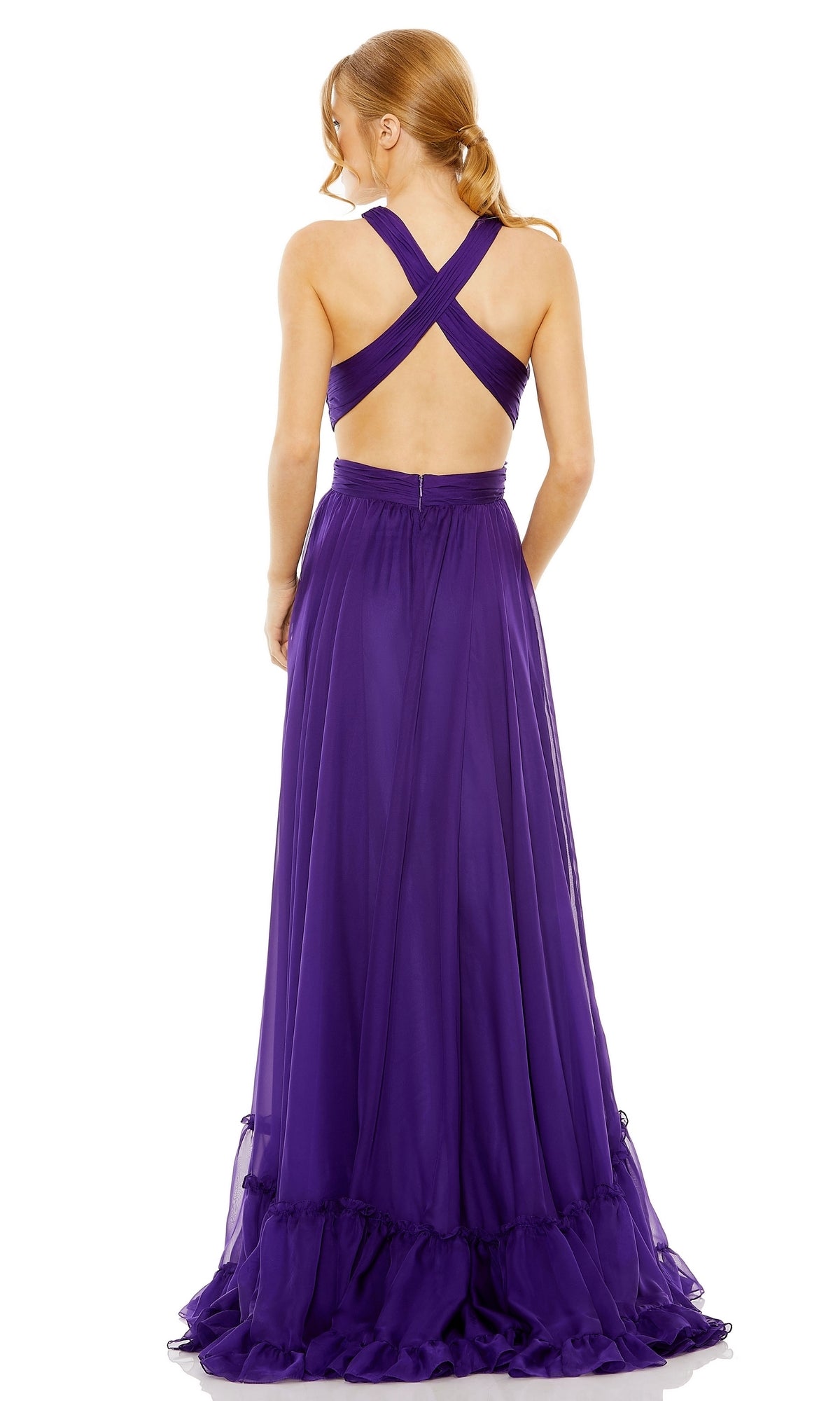 A woman stands facing away, wearing the Long Formal Dress 68474 by Mac Duggal—a floor-length, sleeveless purple gown featuring a crisscross open back.