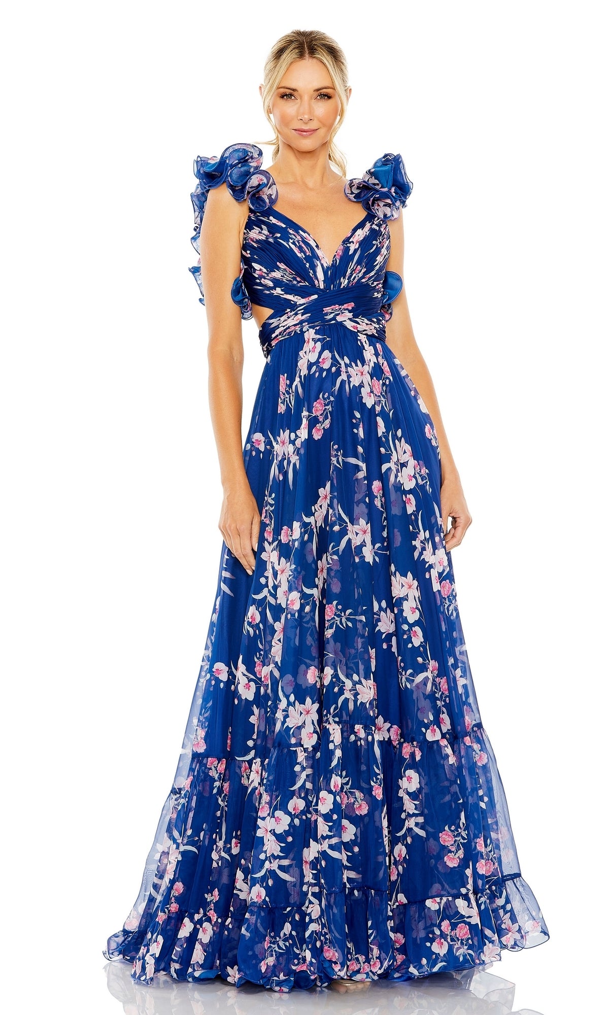 A woman models the Mac Duggal 68520 long blue print formal dress, featuring ruffled sleeves, a deep V-neckline, and side cutouts, standing against a white background.